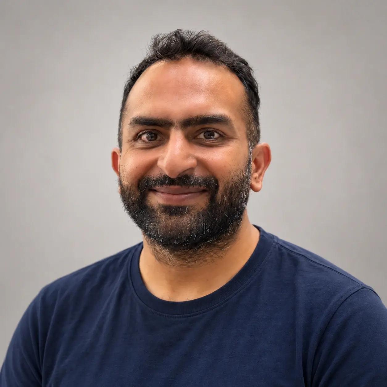 Nivesh Saharan smiling in a navy T-shirt against a grey studio backdrop